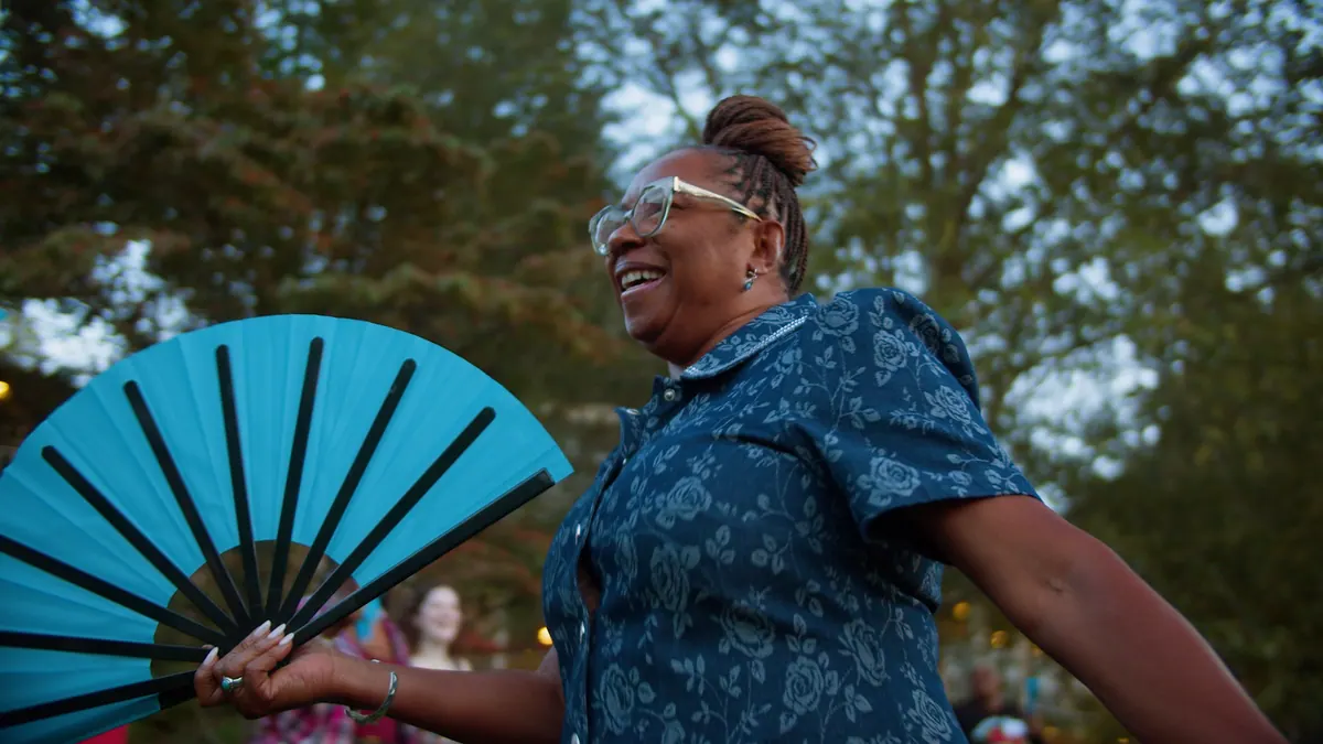 A woman laughing with a teal hand fan at an outdoor event