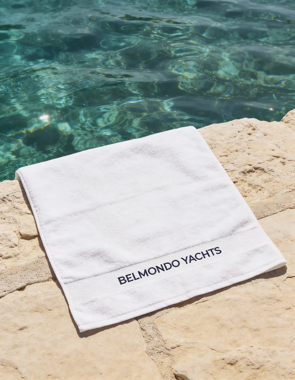 A folded Belmondo Yachts towel on a poolside ledge